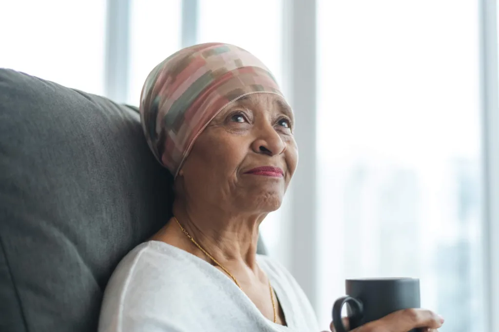 A black senior woman with cancer is wearing a scarf on her head.