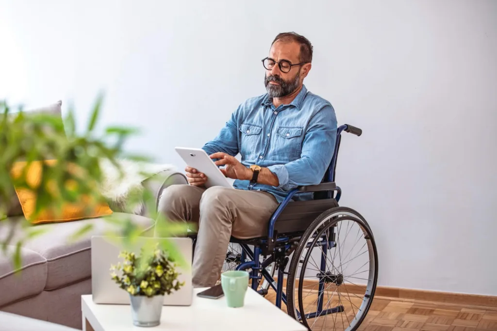 Disabled businessman sitting in a wheelchair at home, holding a digital tablet in hand.